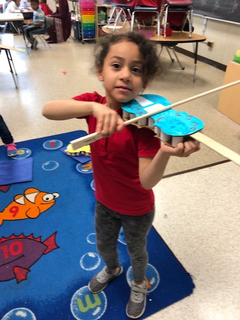 A child holding a cardboard paper violin