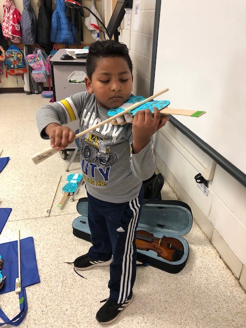 A child holding a cardboard paper violin