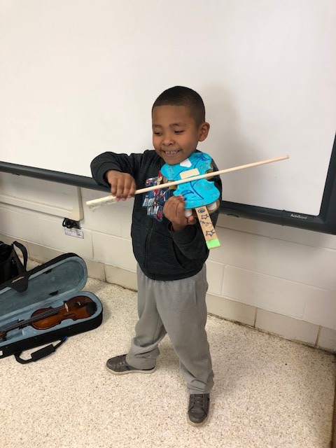 A child holding a cardboard paper violin