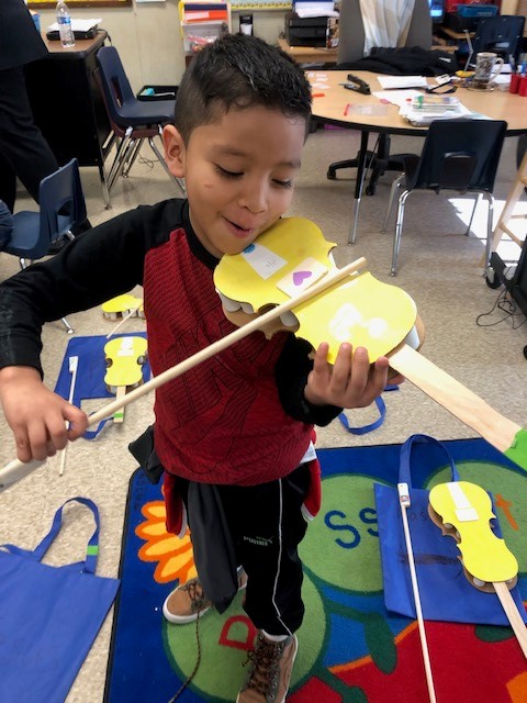 A child holding a cardboard paper violin