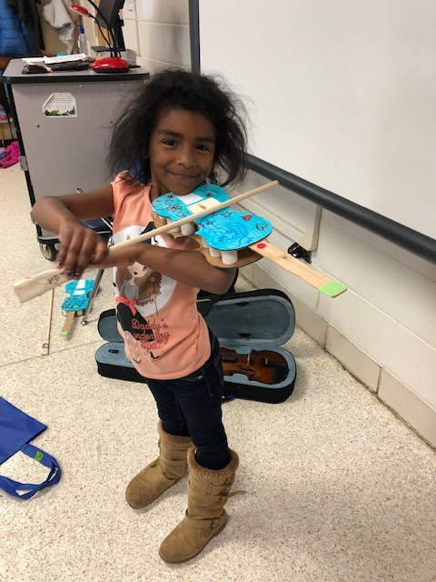 A child holding a cardboard paper violin