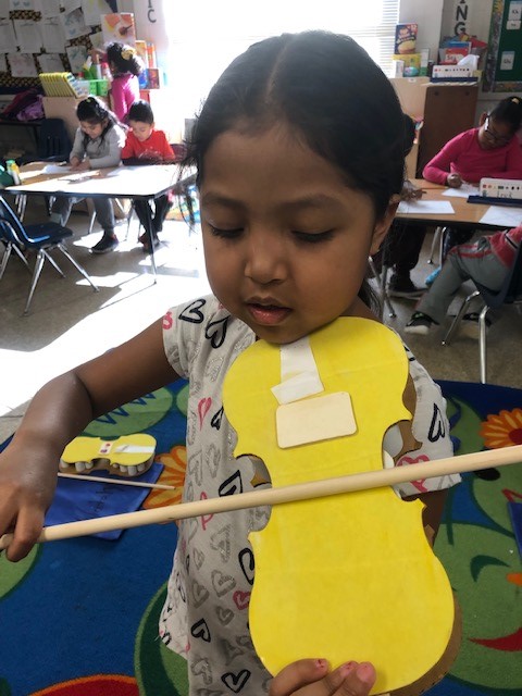 A child holding a cardboard paper violin