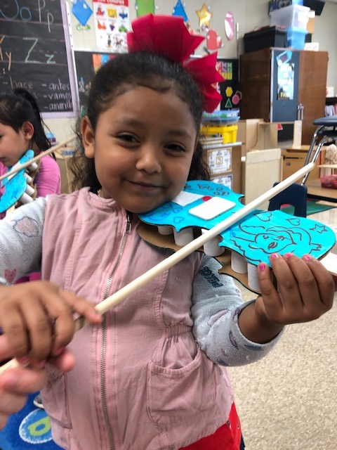 A child holding a cardboard paper violin