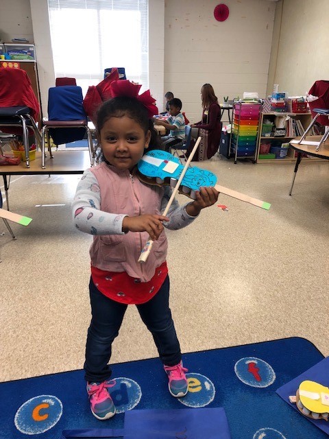 A child holding a cardboard paper violin