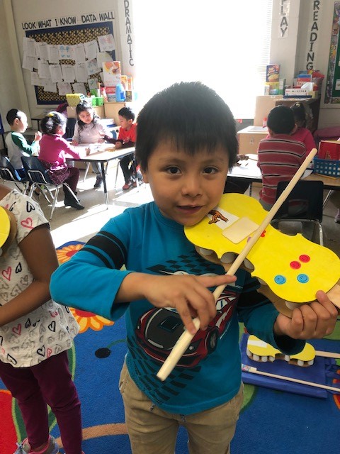 A child holding a cardboard paper violin