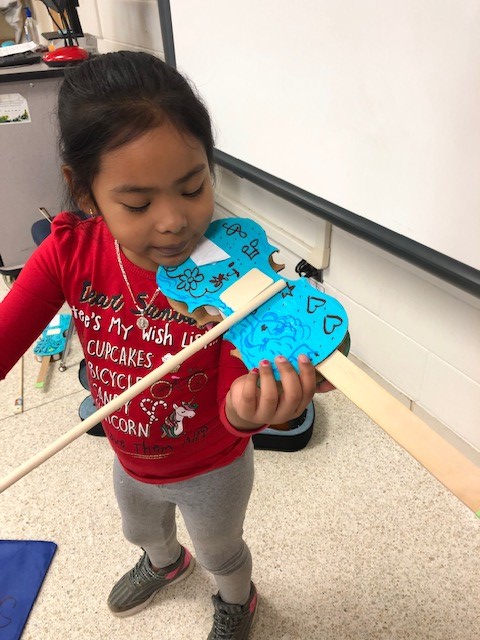 A child holding a cardboard paper violin