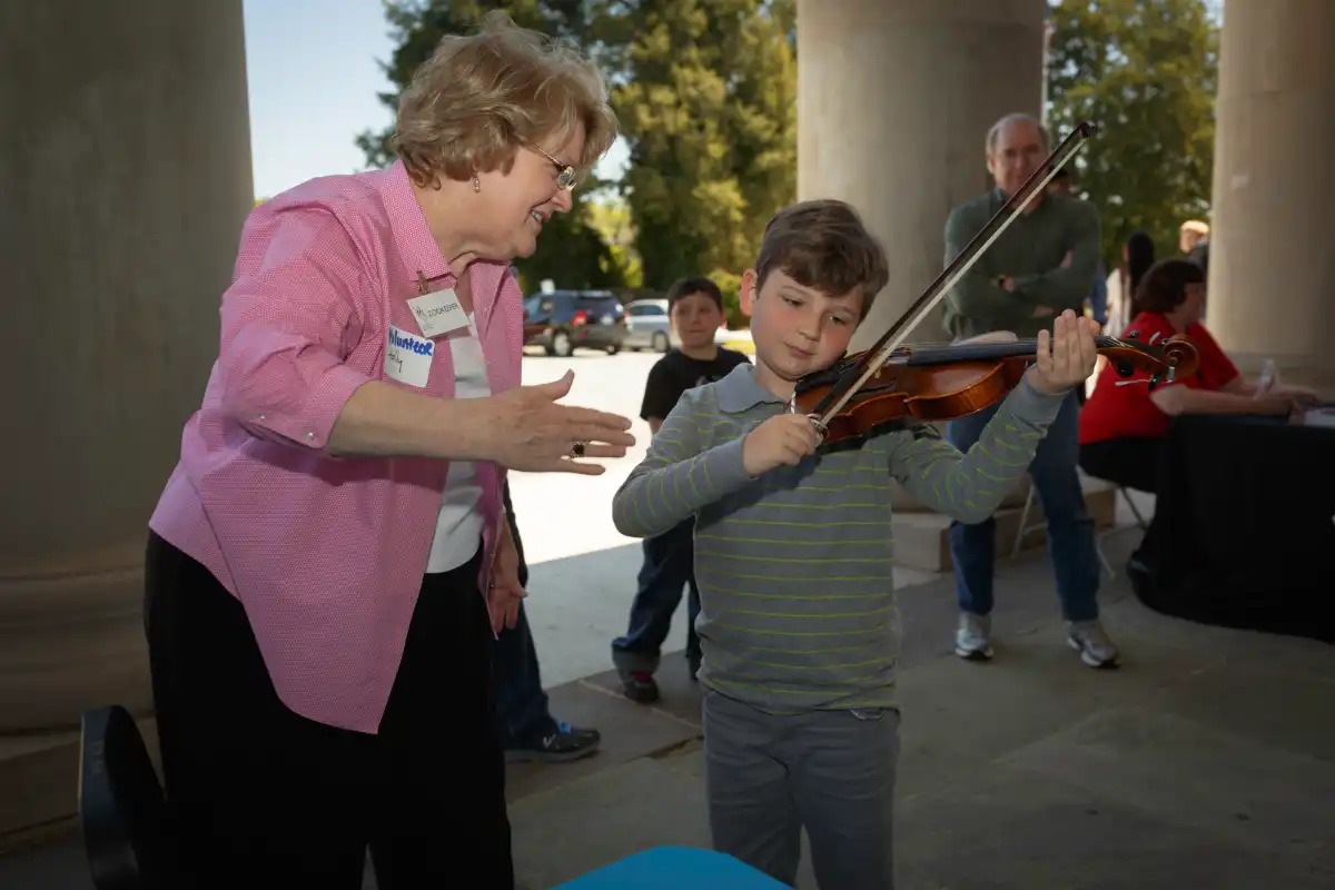 Volunteer helping a child try out the violin at an Ignite Family Concert