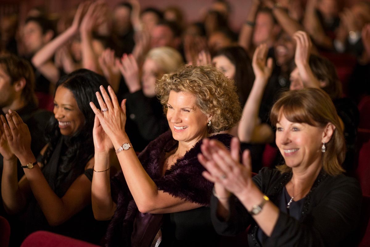 Audience applause at a concert, focused on a blonnd woman with curly hair.